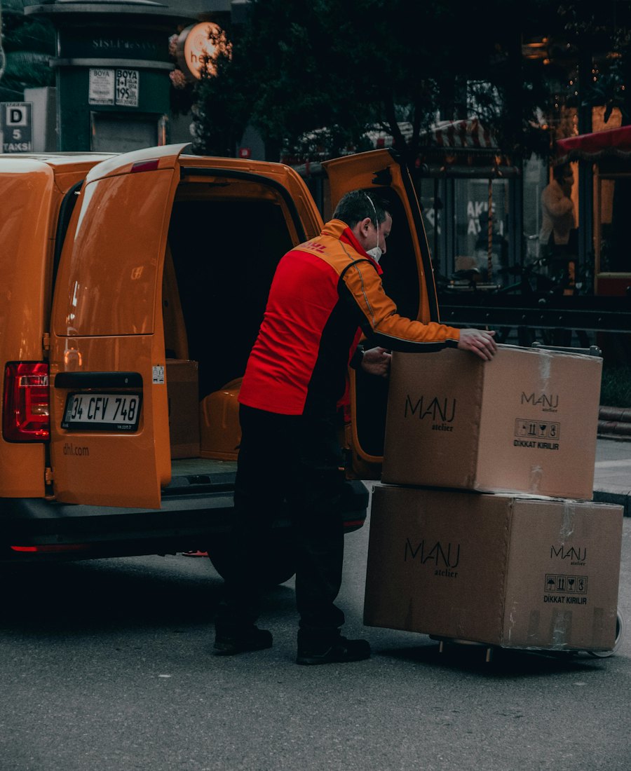 A courier loading cardboard boxes into an orange delivery van